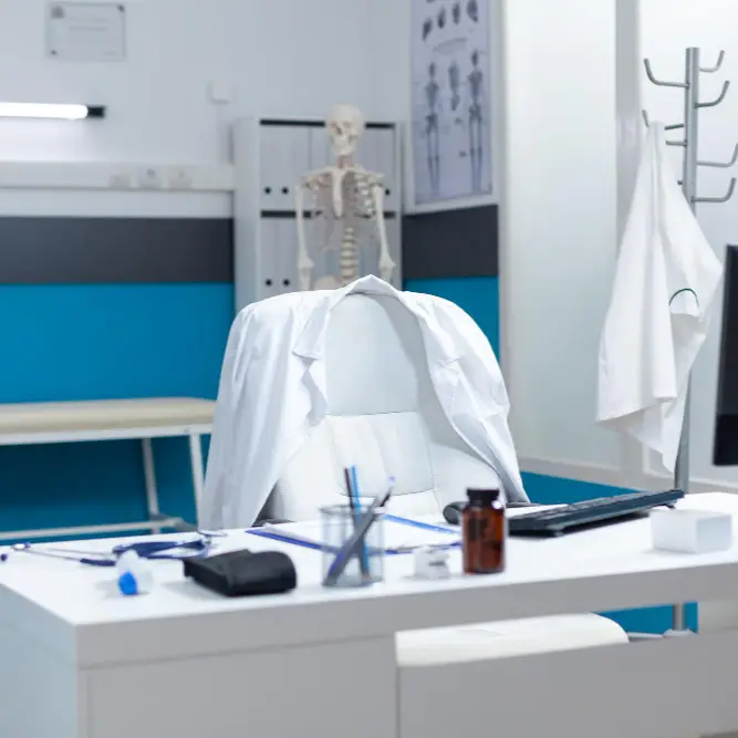 Empty chair at a desk with doctors jacket hanging over the back of the chair