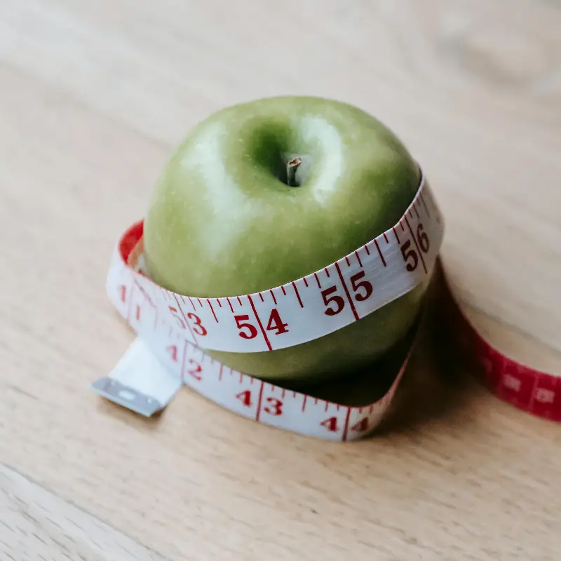 A green apple encircled by a measuring tape, symbolizing diet and fitness goals.